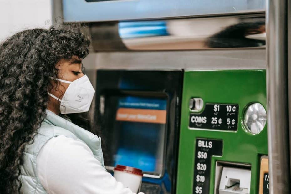 a woman wearing a face mask uses a ticket machine for purchasing fare in a public setting reflectin